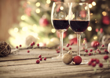 Christmas holiday red wine on a rustic wooden table in front of a Christmas tree. Very shallow depth
