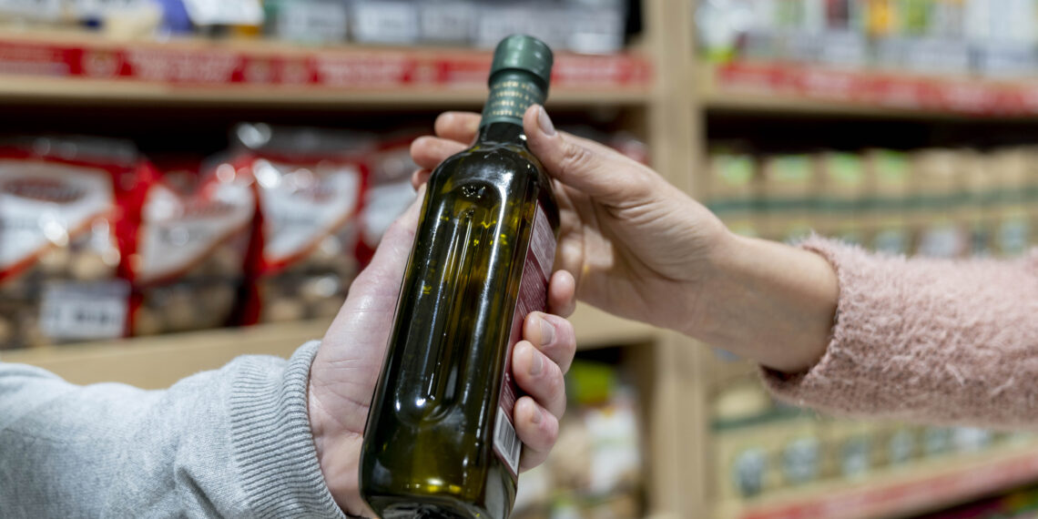 Unrecognizable customer handing an olive bottle oil to partner - Close up