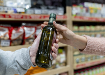 Unrecognizable customer handing an olive bottle oil to partner - Close up